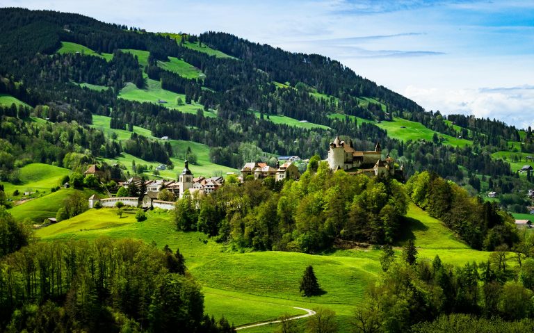 Aerial shot of Gruyères Castle nestled in the lush green landscape of Switzerland.