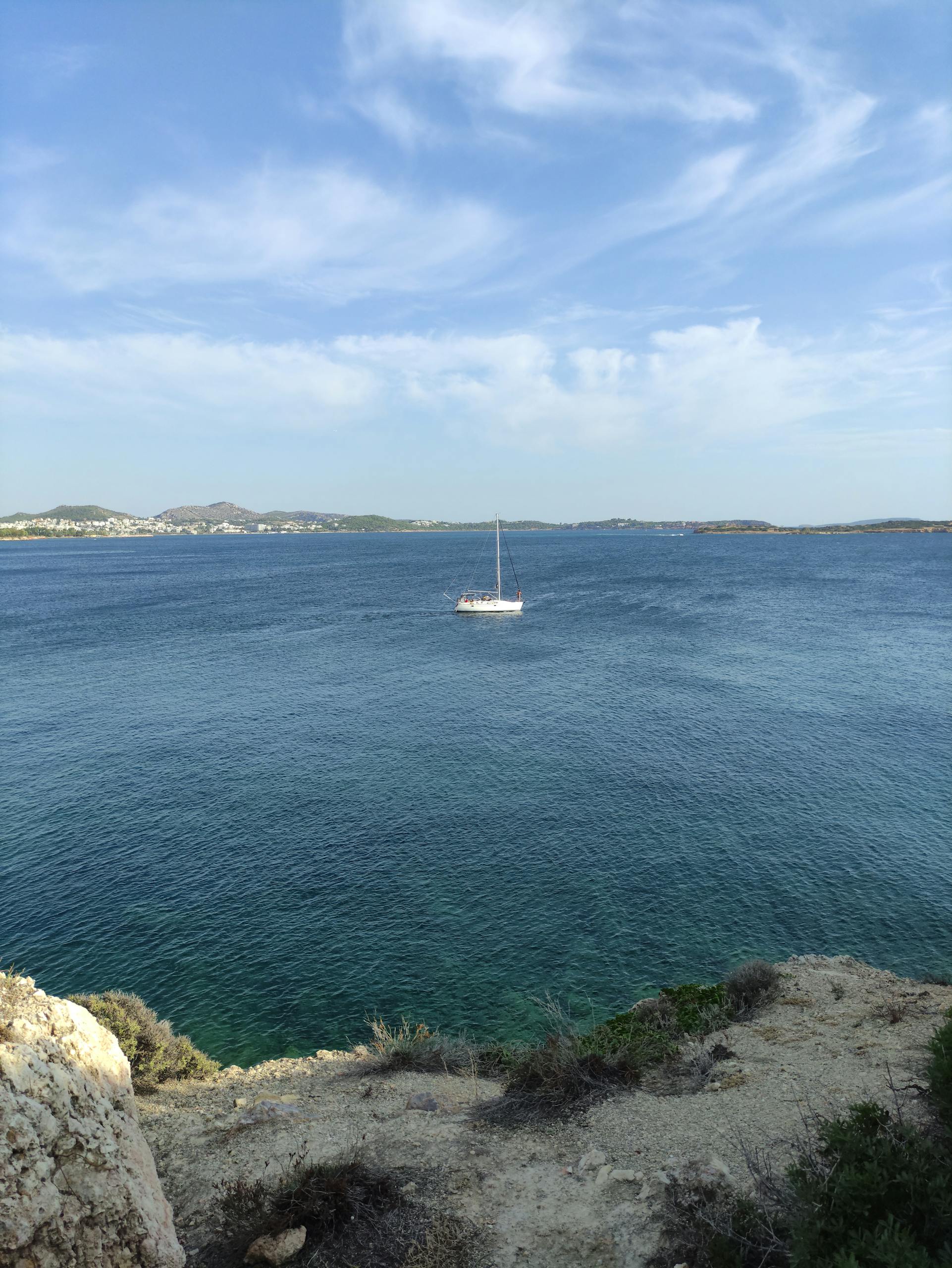 A serene view of a sailboat drifting on the blue waters of the Aegean Sea from Voula, Greece.