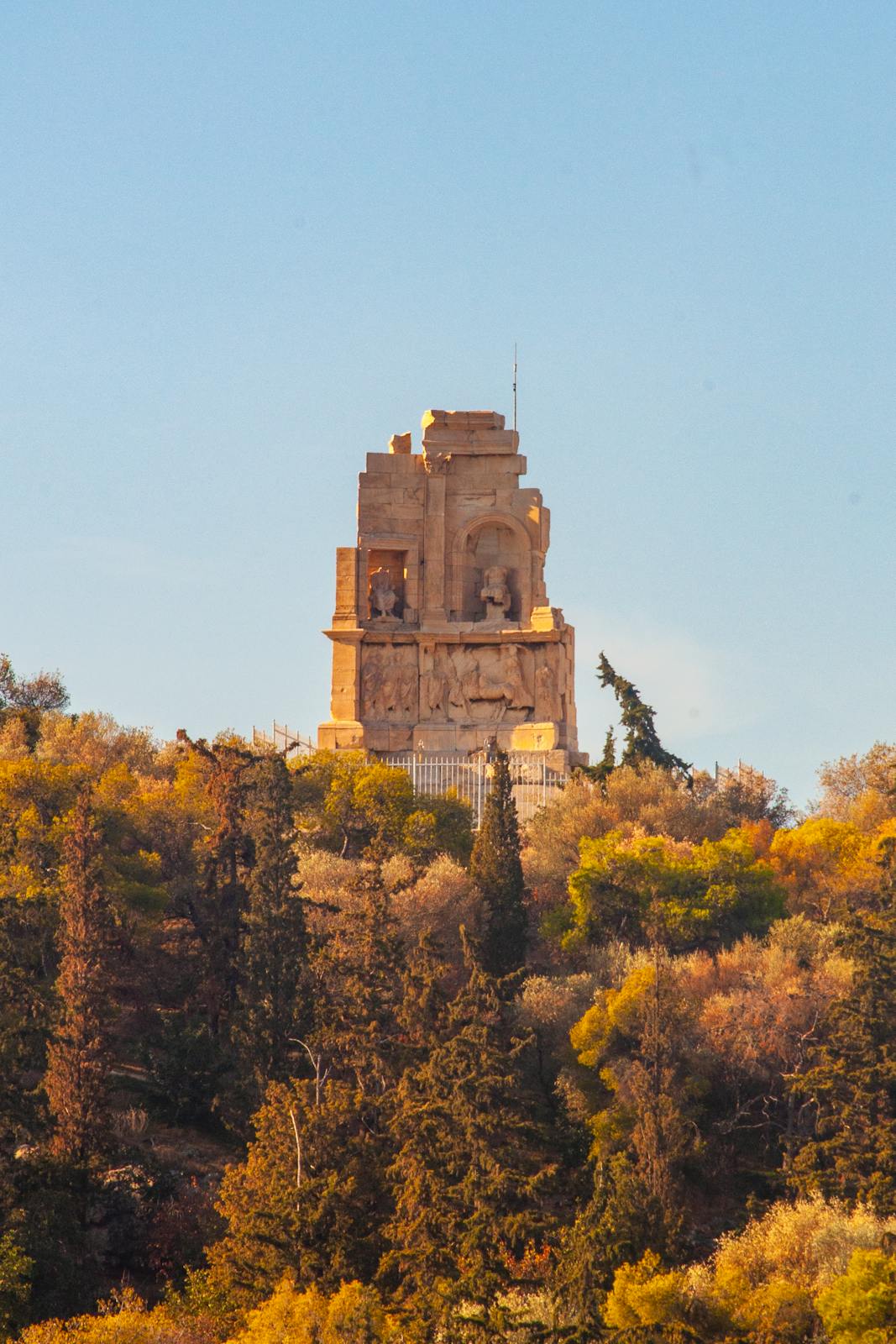 A stunning view of the Philopappos Monument surrounded by fall foliage in Athens, Greece.