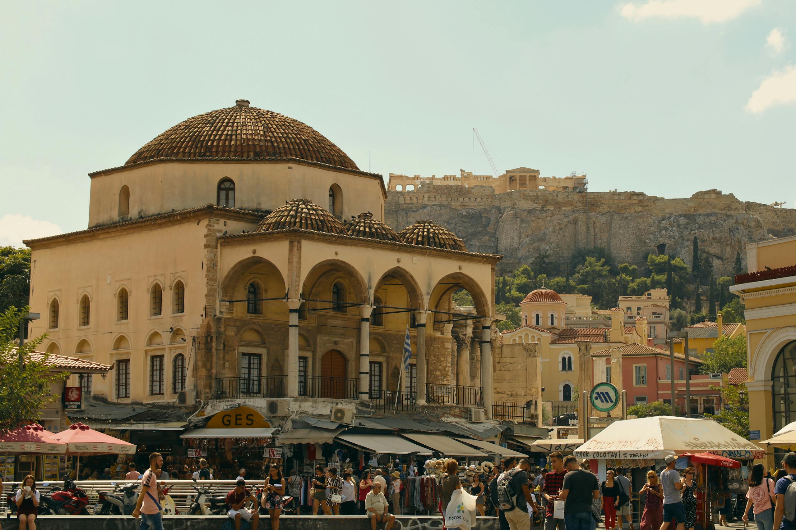 Bustling Monastiraki Square in Athens with the iconic Acropolis in the background.