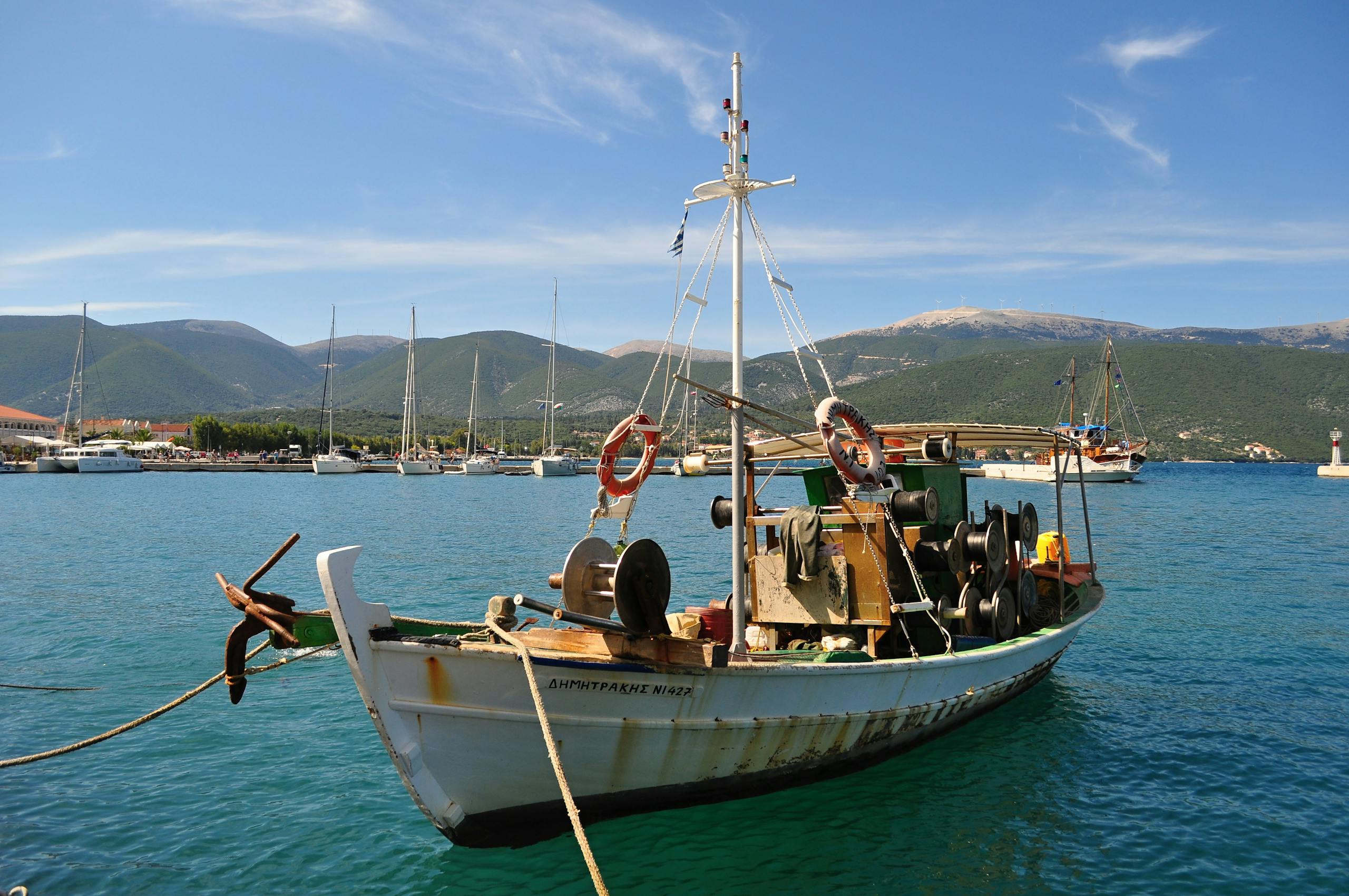 A traditional fishing boat docked in a scenic coastal Greek harbor with mountains.