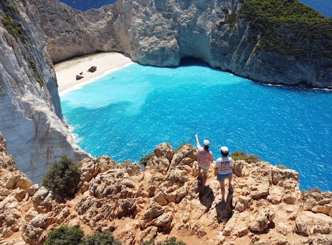 Maria and Olivia on cliff's edge overlooking turquoise sea waters