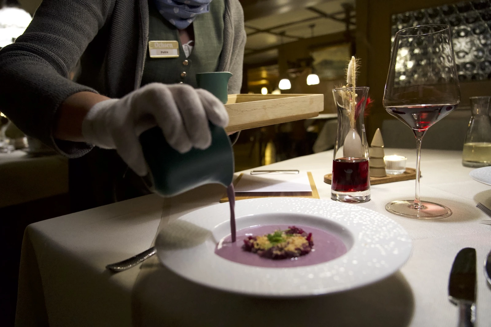 waiter wearing white gloves pours soup into bowl at a german restaurant