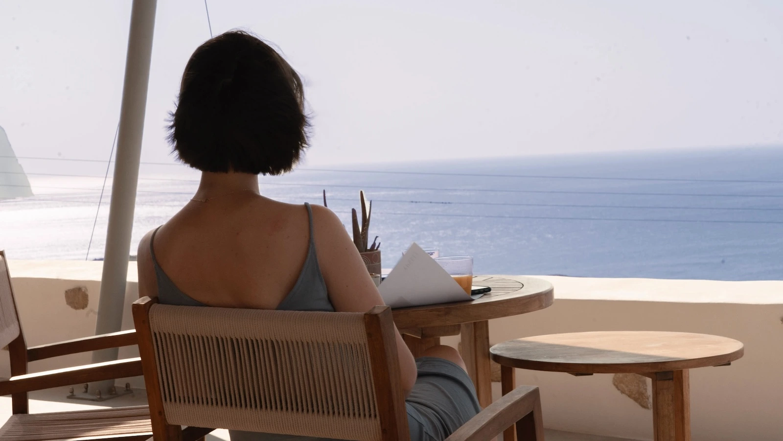 girl with short hair overlooking the aegean sea while seating at a table for breakfast