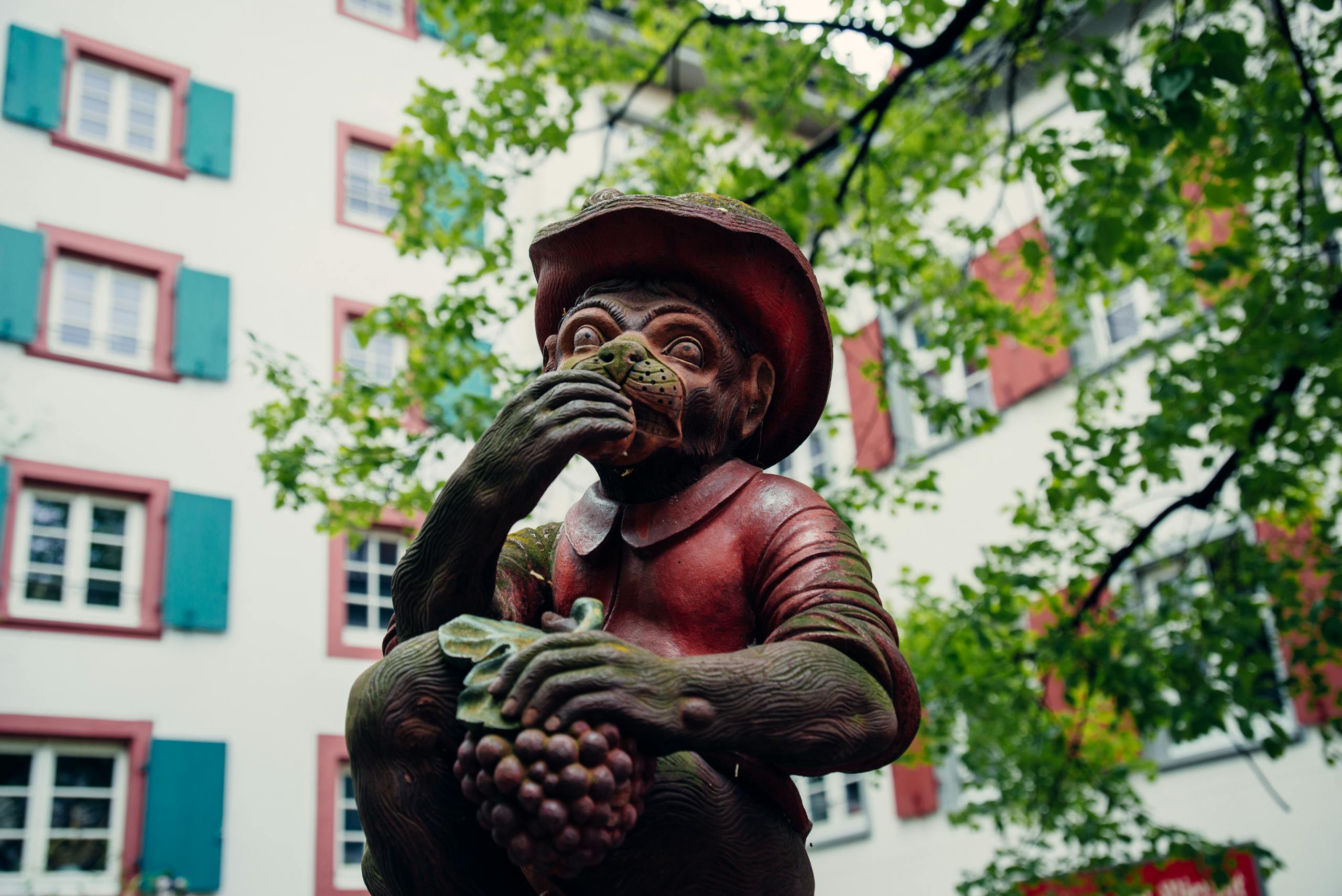 A charming monkey statue holding grapes, set against Basel's unique city architecture.